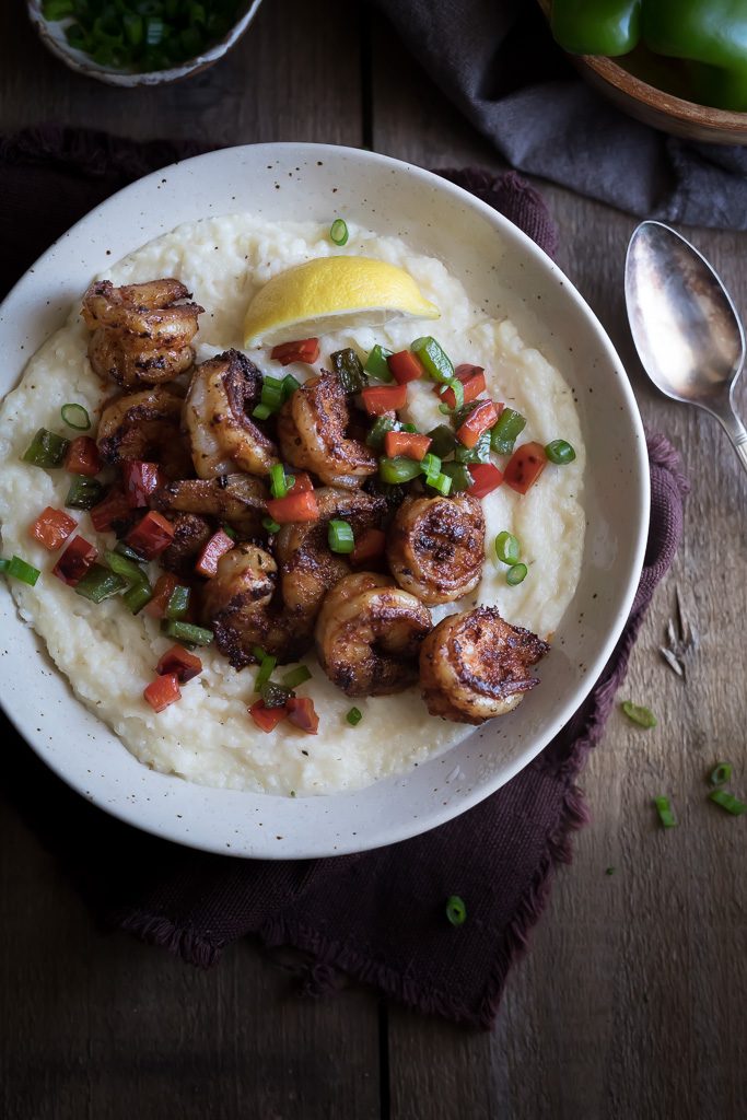 A big bowl of the delicious Cajun Shrimp and Grits served on top of mashed potatoes with some green onions and bell peppers on the side