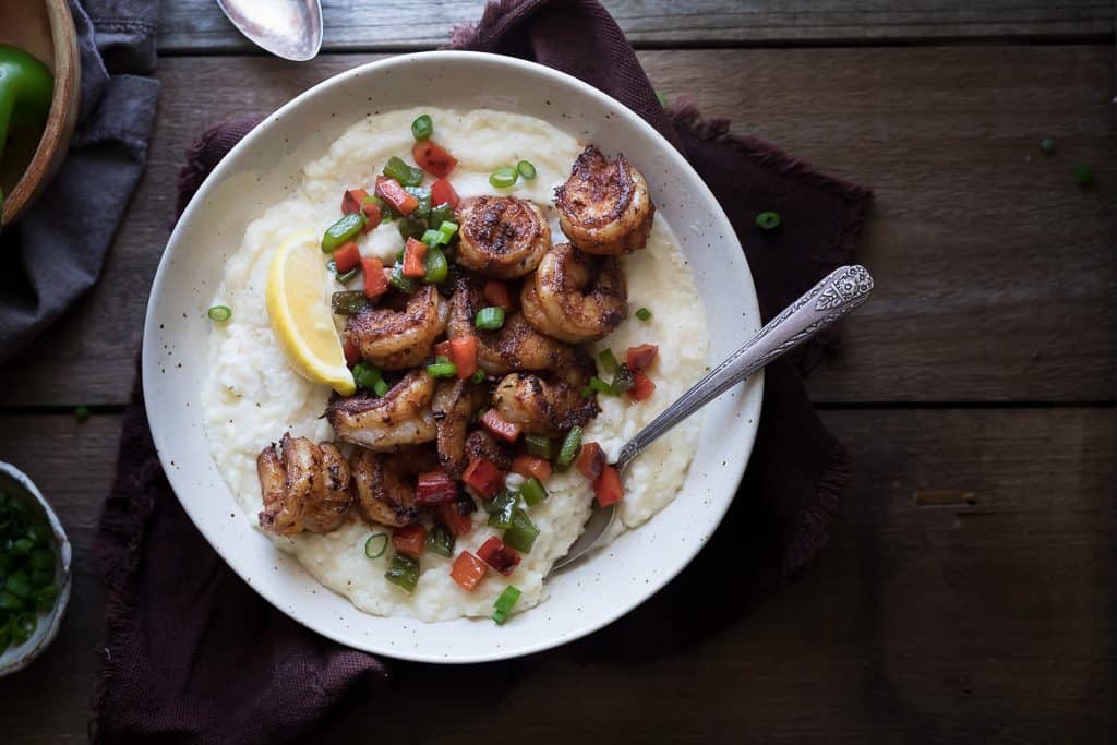 Overhead on the mouthwatering Cajun Shrimp and Grits in a white plate on a wooden table