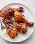 Cooked BBQ chicken legs on white plate with fork.