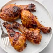 Cooked BBQ chicken legs on white plate with fork.