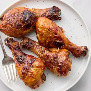 Cooked BBQ chicken legs on white plate with fork.