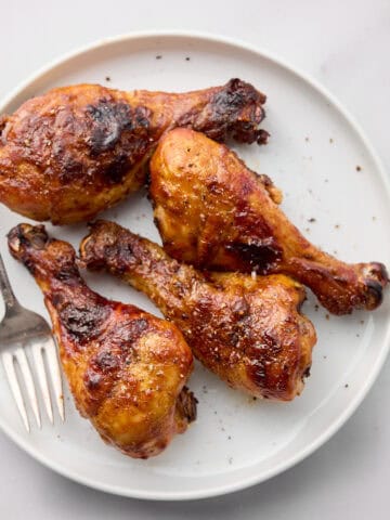Cooked BBQ chicken legs on white plate with fork.