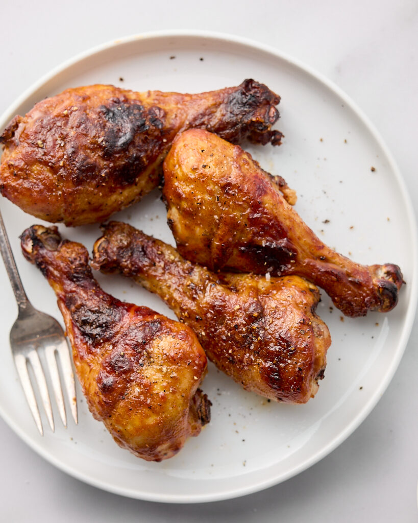 Cooked BBQ chicken legs on white plate with fork. 