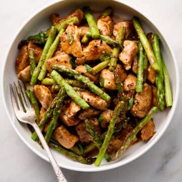 Chicken and asparagus stir fry in white bowl with fork.