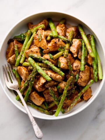 Chicken and asparagus stir fry in white bowl with fork.