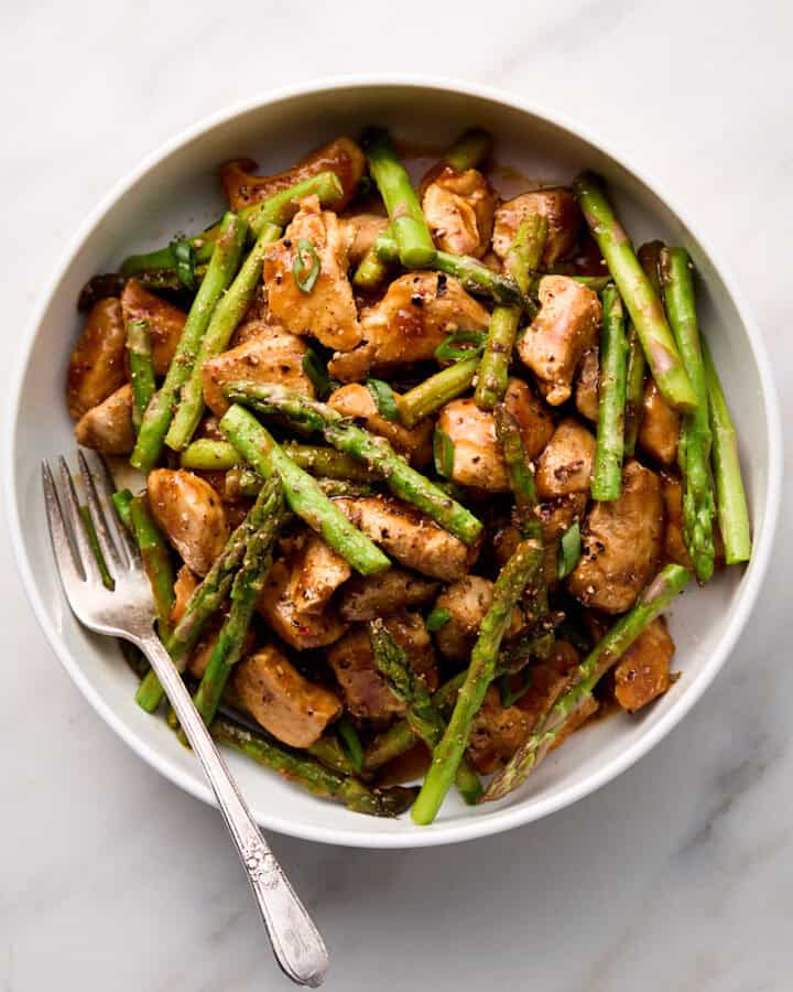 Chicken and asparagus stir fry in white bowl with fork.