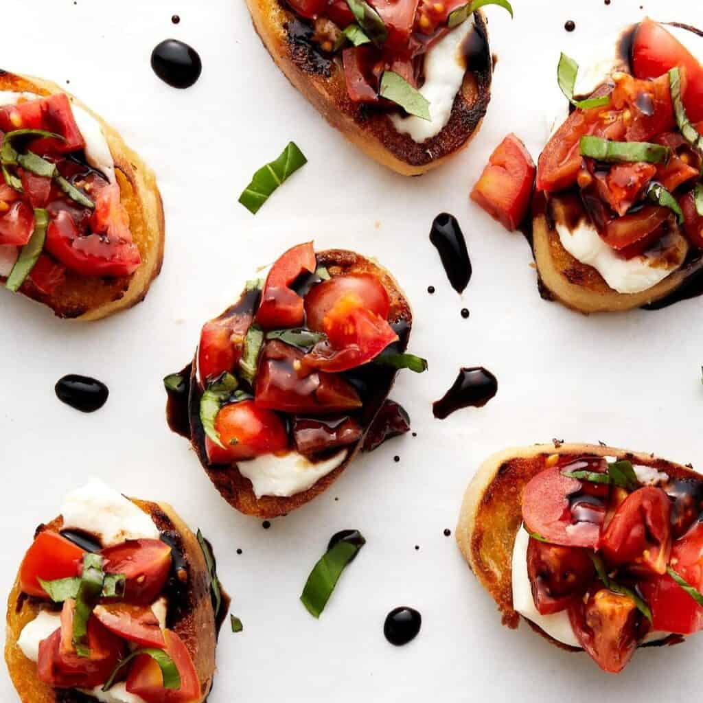 Bruschetta pieces with basil on white parchment paper.