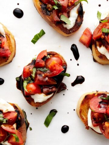 Bruschetta pieces with basil on white parchment paper.
