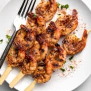 Cooked shrimp skewers on white plate with fork.