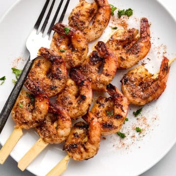 Cooked shrimp skewers on white plate with fork.