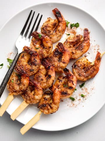 Cooked shrimp skewers on white plate with fork.