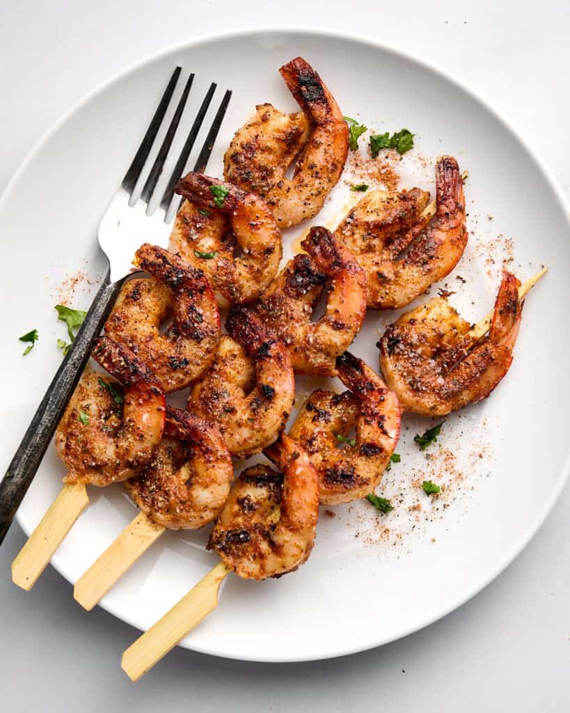 Cooked shrimp skewers on white plate with fork.