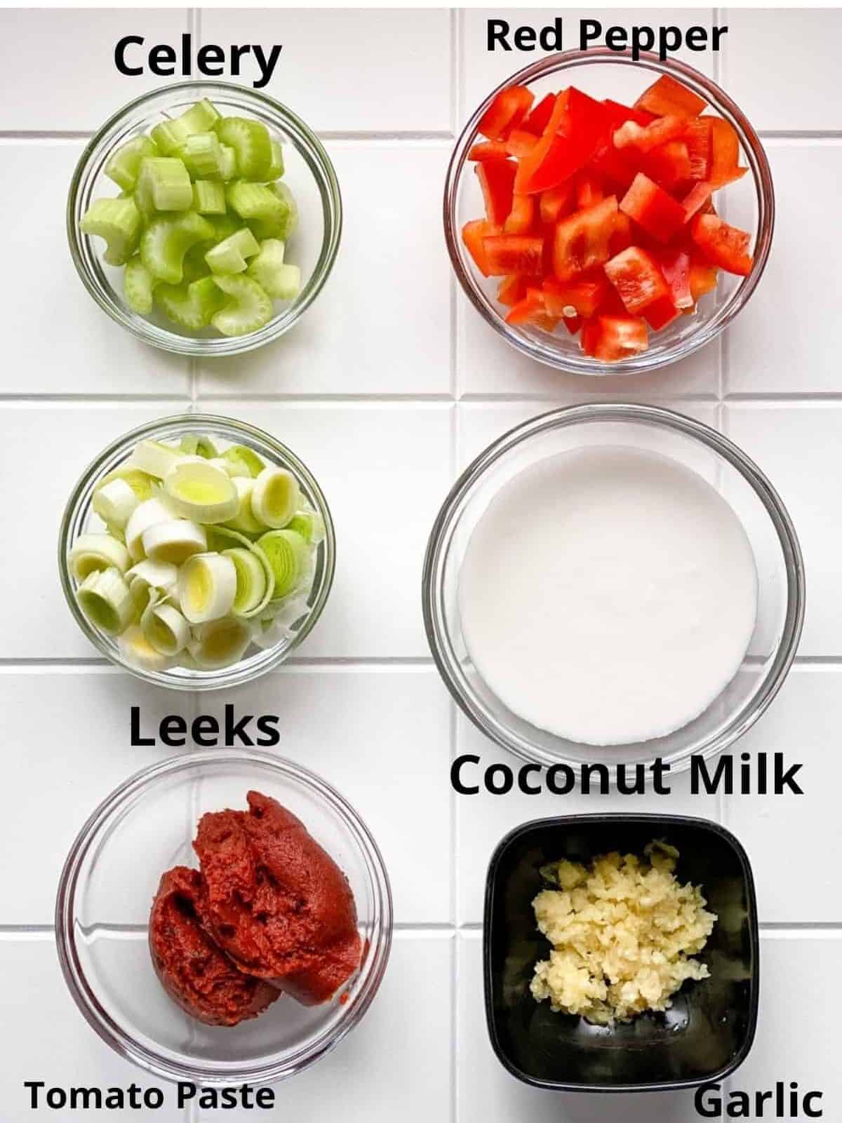 Creamy seafood ingredients in bowls on white board including milk leeks celery tomato paste and peppers