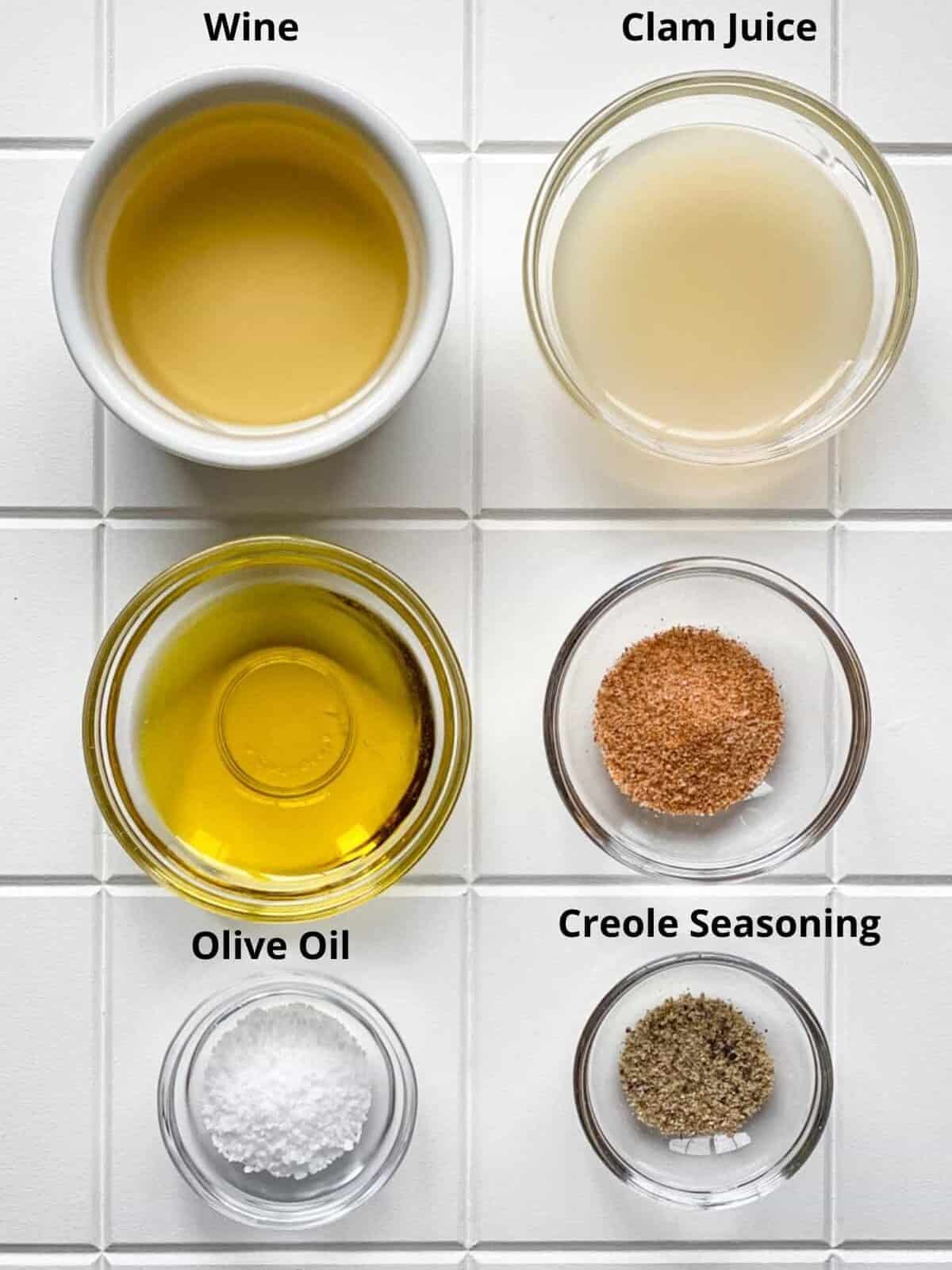 Ingredients wine clam juice olive oil creole seasoning salt and pepper in bowls on white board.
