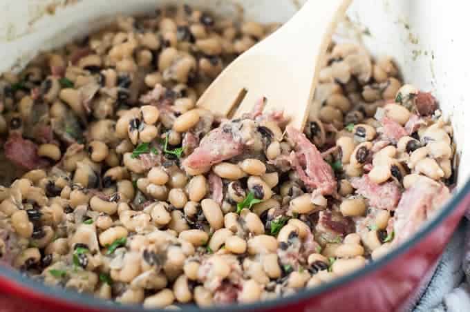 A big pot of Spicy and Smoky Southern Black Eyed Peas with a wooden ladle inside