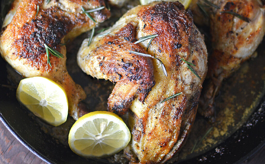 Cooked chicken with lemon and rosemary in pan.