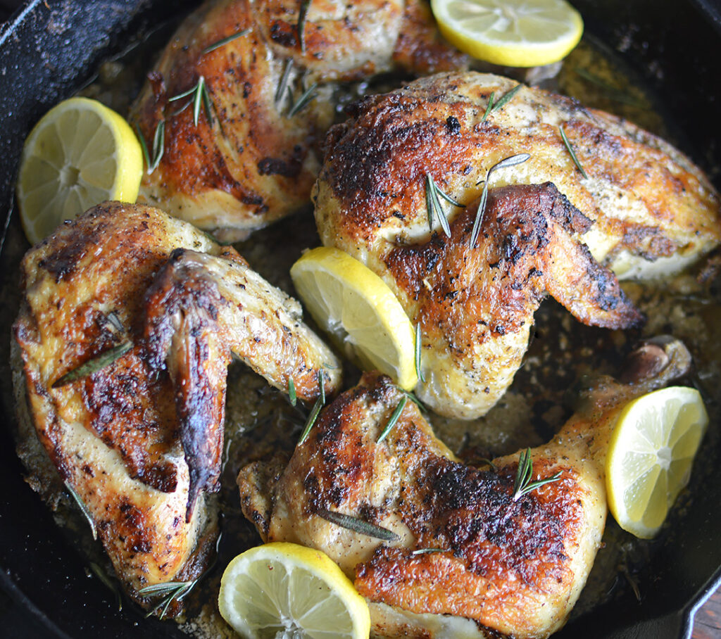 Cooked chicken with lemon and rosemary in pan.