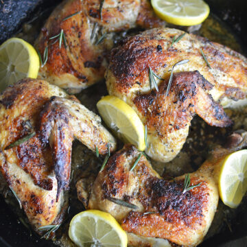 Cooked chicken with lemon and rosemary in pan.