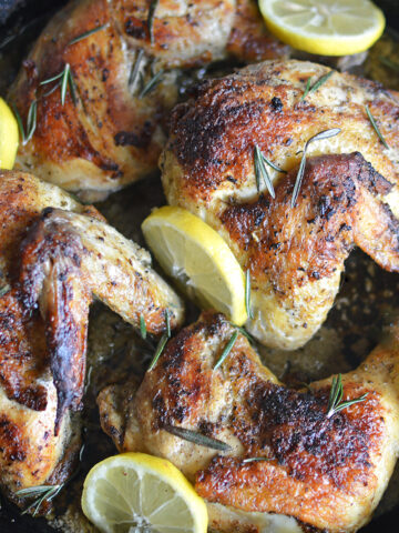 Cooked chicken with lemon and rosemary in pan.