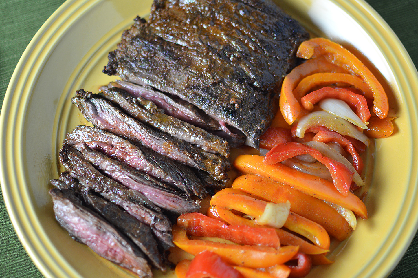 Citrus Marinated Skirt Steaks served with red peppers on a big yellow plate