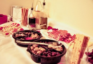 With our Italian themed night, what better than an antipasti bar! Placing some items in wine glasses help set off both themes. And olives from the local grocery stayed in their tray from the store because they went with the colors, saving me time and money regarding serving trays. I also bought plastic reusable serving trays that you see here also. They have been use for other parties as well. Look around your house for those olive oil dispensers and used wine bottles from the other night to help decorate.