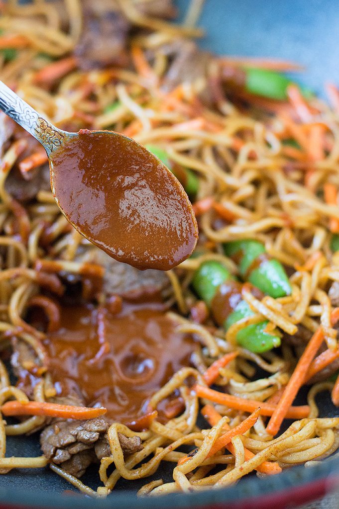 A spoonful of tasty and spicy red curry sauce over a bowl full of the delicious Stir Fried Thai Red Curry Noodles with Beef