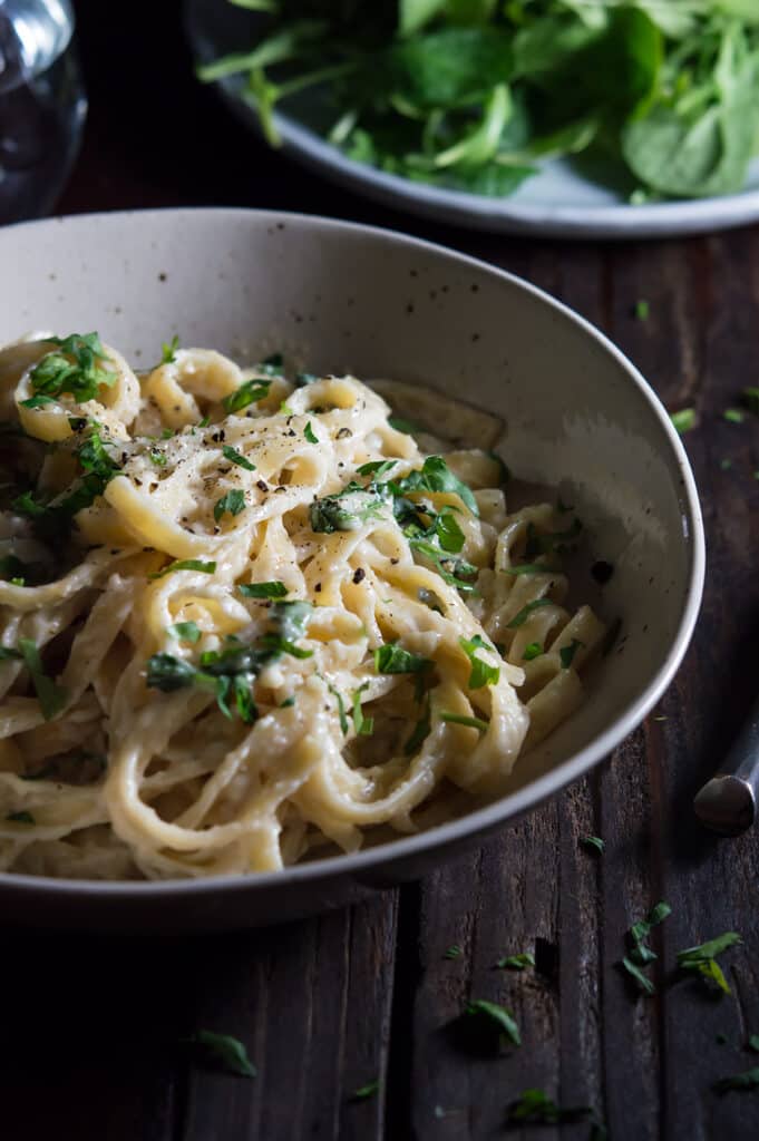 Asiago Cream Sauce Pasta served in big nice bowl with extra spinach blurred in the background