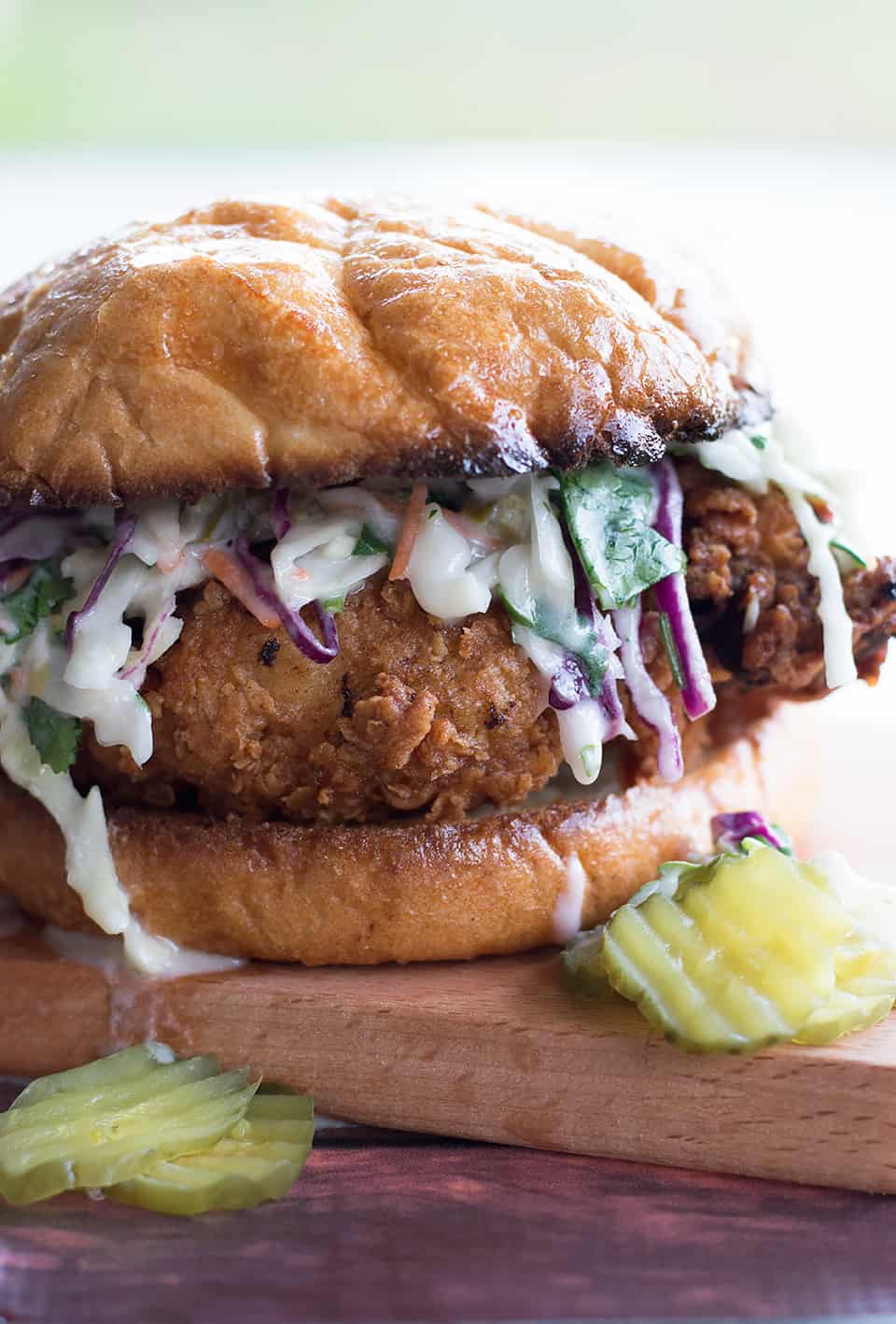 Buttermilk Fried Chicken Sandwich with Cilantro Jalapeño Coleslaw served on a wooden board with pickles on the side