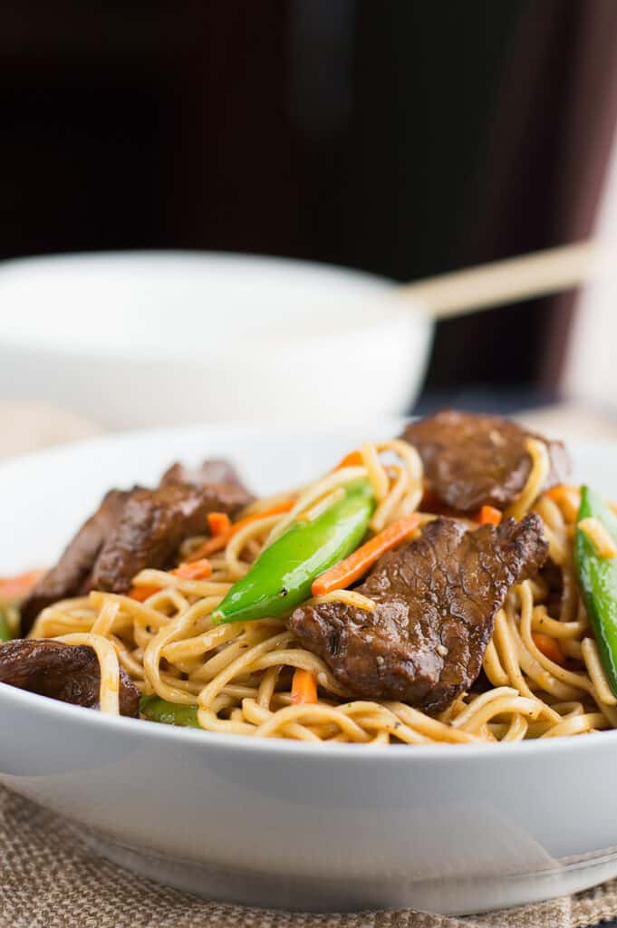 Closeup of a white bowl full of the homemade Stir Fried Thai Red Curry Noodles with Beef with another bowl blurred in the background