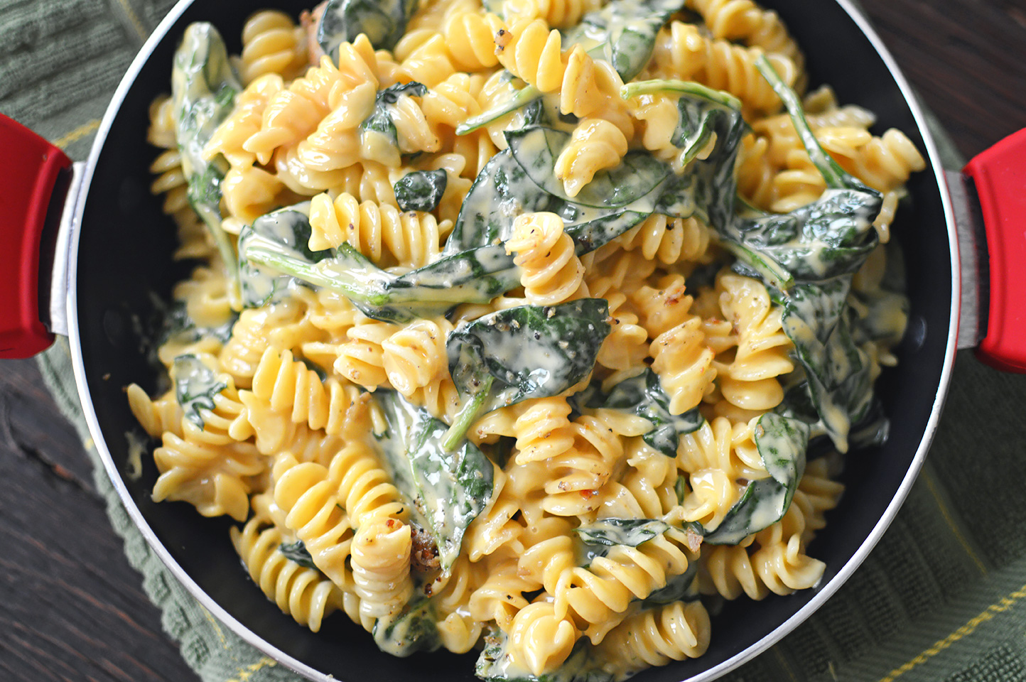 Overhead on the delicious Cheesy Chicken and Spinach Pasta presented in a big pan with red handles