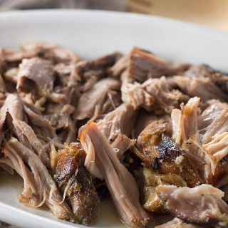 Closeup of the mouthwatering Slow Cooker Kalua Pig looking juicy and absolutely invitin on a white plate with a wooden spoon right next to it