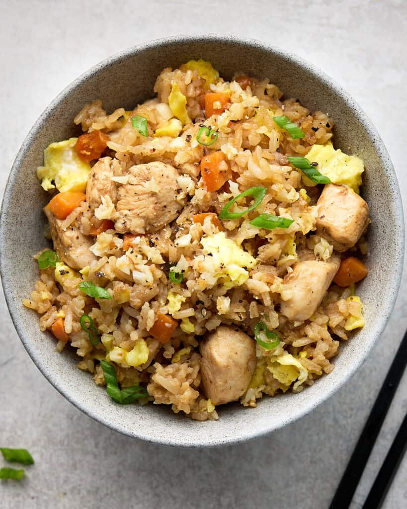 Fried rice with chicken and vegetables in gray bowl with chop sticks.
