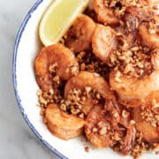 Shrimp garlic and lemon in bowl on white marble table with lemon wedges on table.