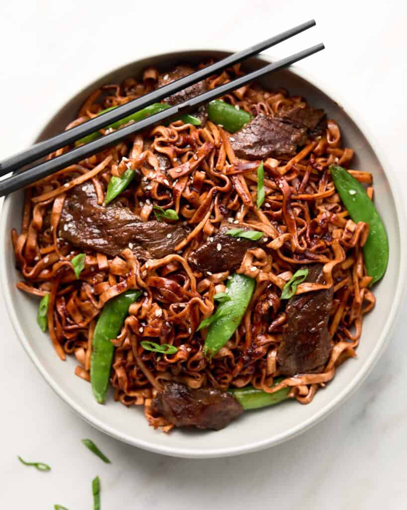 Red Thai Curry Beef Noodle stir fry in white bowl with chopsticks