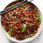 Red Thai Curry Beef Noodle stir fry in white bowl with chopsticks
