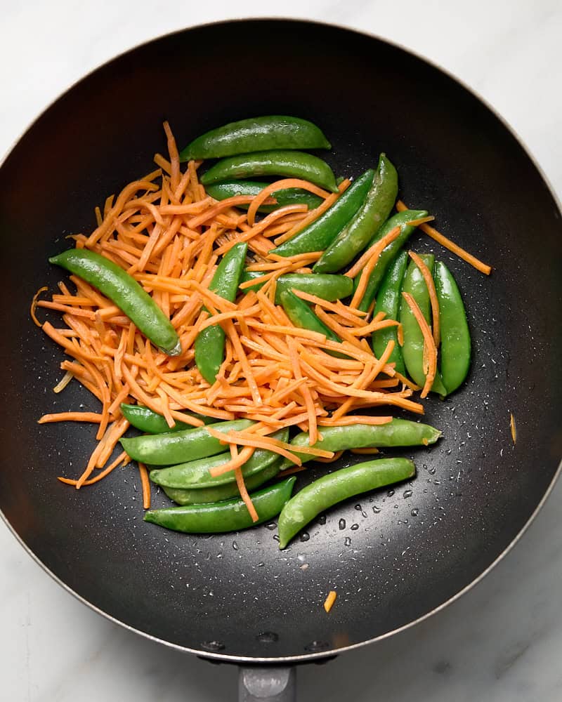 Sugar snap peas and shredded carrots in wok.