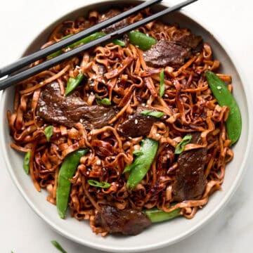 Red Thai Curry Beef Noodle stir fry in white bowl with chopsticks