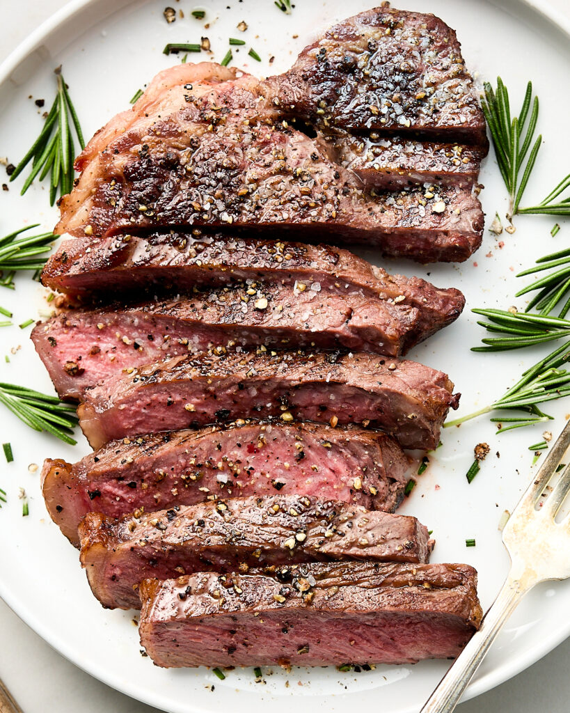 Cooked steak with rosemary garnish on white plate with fork.