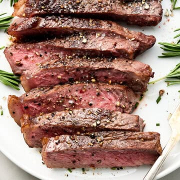 Cooked steak with rosemary garnish on white plate with fork.