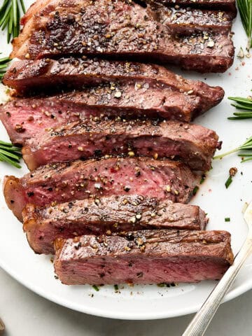 Cooked steak with rosemary garnish on white plate with fork.