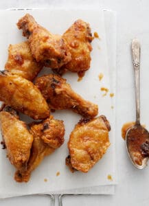Wings on white paper and metal rack with parsley and spoon.