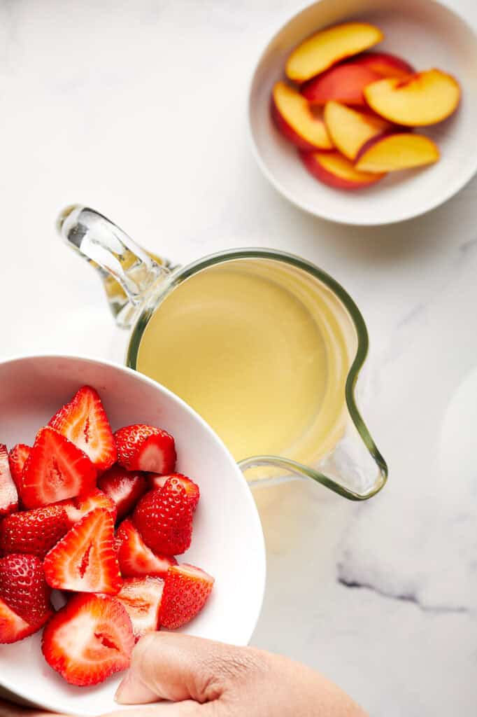 Adding Strawberries to pitcher of wine for Sparkling Peach and Strawberry Sangria