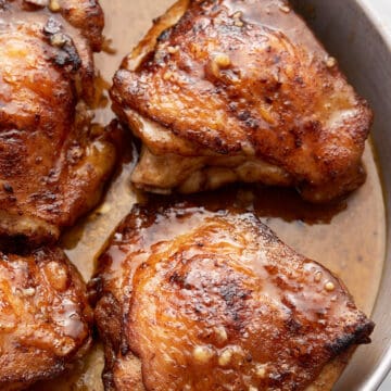 Chicken in metal pan with small bowl of seasoning spoon and napkin on white table.