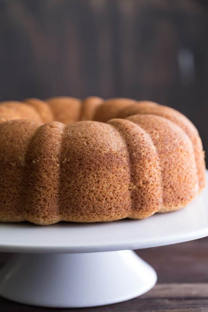 Side closeup on the Delicious Amaratto Bundt Cake with the perfect texture, presented on a cute white stand with a dark background
