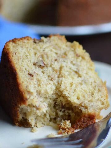 A big piece of the Easy Banana Bread Cake served in a white plate with a metal fork on the side
