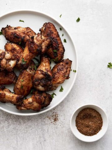Wings on white plate with garnish and small white bowl of spices.