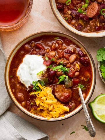 Two bowls of chili surrounded by a napkin, glass of drink, and lime and parsley garnish.