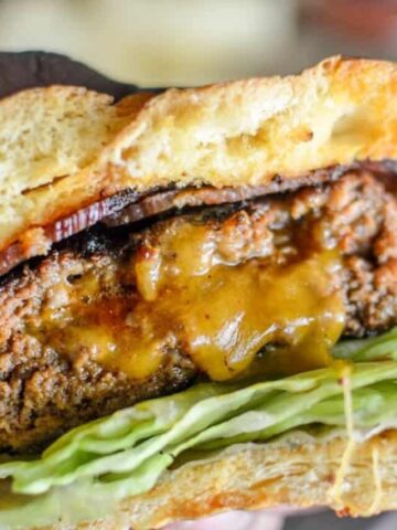 Holding cooked Cheese Stuffed Chorizo Burgers in the hand in-between the buns with lettuce