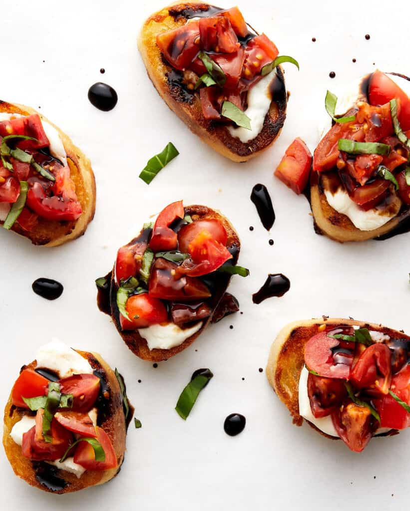 Bruschetta pieces garnished with basil on white parchement paper.