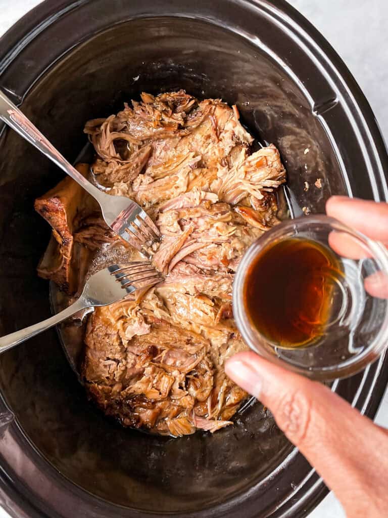 pouring liquid smoke on cooked kalua pork in slow cooker